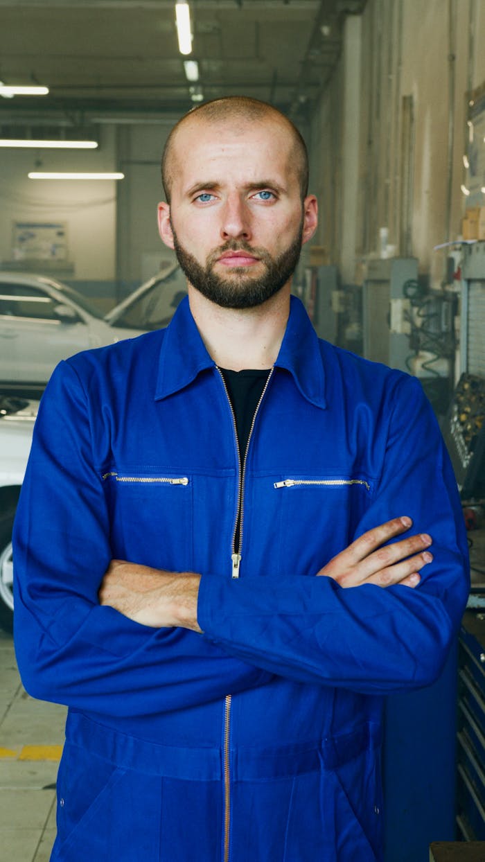 Professional mechanic in blue uniform standing in a garage with arms crossed. Focused and skilled representation.